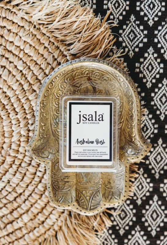 Packet of Jsala soy wax melts sitting in brass hand dish on textured background.