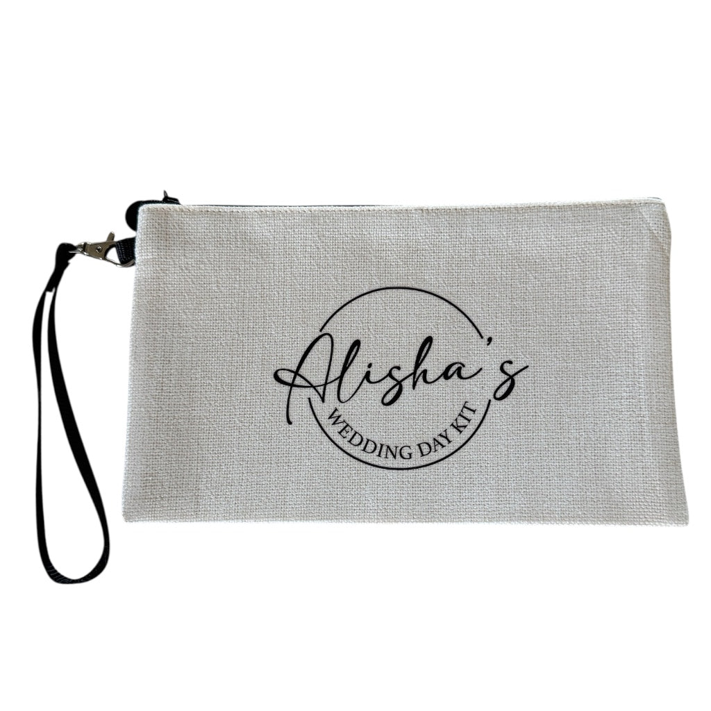 Personalised linen-look clutch bag with the name “Alisha’s” and the words “Wedding Day Kit” printed in black, featuring a black wrist strap and zipper.